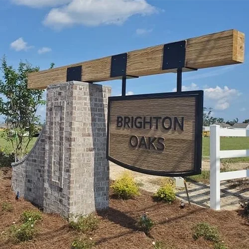 Brick and wood monument sign reading BRIGHTON OAKS at neighborhood entrance under blue sky