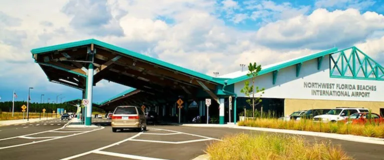 Entrance and drop-off lanes at NORTHWEST FLORIDA BEACHES INTERNATIONAL AIRPORT under teal roof on a sunny day
